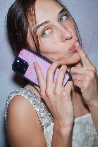 A woman holds a pink phone case in a sparkly dress