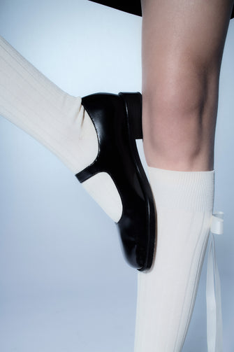 Black spazzolato leather Mary Jane shoes with a buckle closure and a stacked heel against a white background on a model