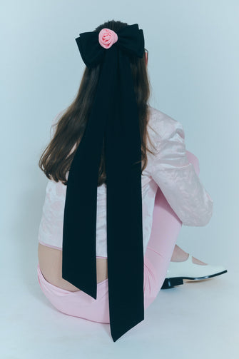 A model wears an elongated black crepe bow with a pink rosette in the center against a white background