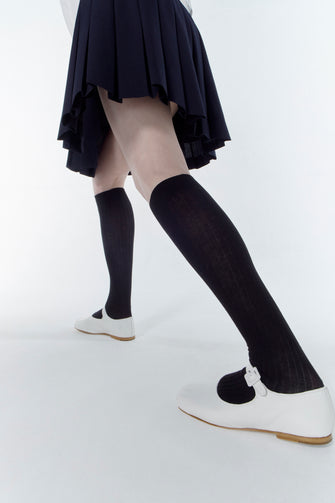 a model wears A single white Mary Jane pointed-toe flat shoe made of Nappa leather, featuring an adjustable pin-buckle strap and a padded leather footbed against a white background