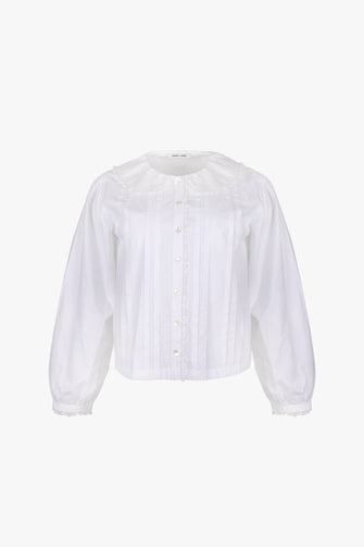 A long-sleeved white cotton blouse with tonal embroidery detail at the collar, mother of pearl buttons at the front, and lace trim throughout against a white backgorund