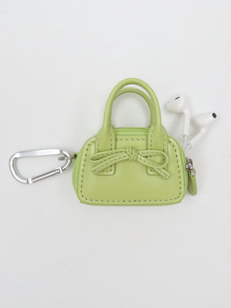 Green handbag-shaped keychain with a bow featuring headphones poking out of bag on a white background