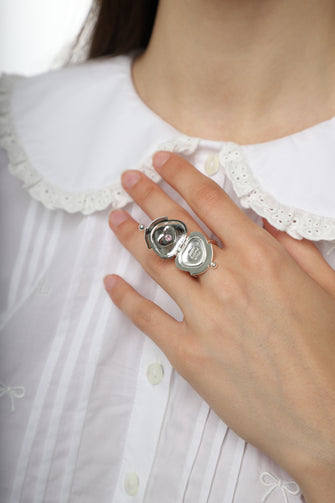 Close-up of a hand wearing a silver urse shaped ring with a locket design on a white background