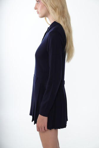 A woman wears a navy mini sweater dress with long sleeves and a polo neck. It features mother of pearl buttons against a white background
