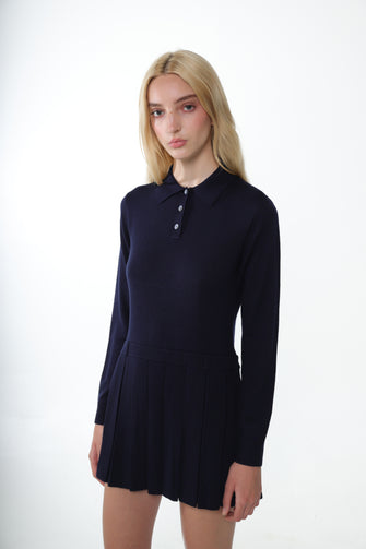 A woman wears a navy mini sweater dress with long sleeves and a polo neck. It features mother of pearl buttons against a white background