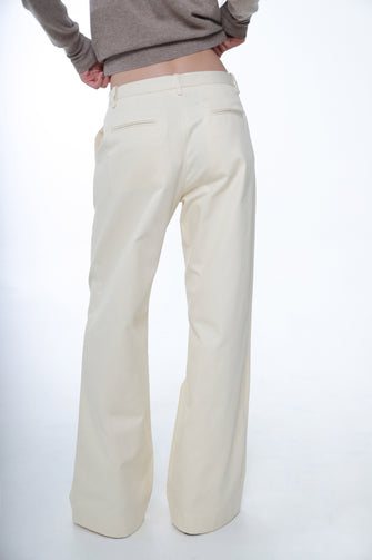 A woman wears a tan sweater and a full length cotton trousers in cream color, wide leg fit, and low waist with yellow shoes against a white background