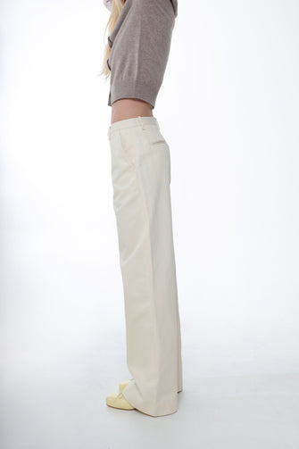 A woman wears a tan sweater and a full length cotton trousers in cream color, wide leg fit, and low waist with yellow shoes against a white background