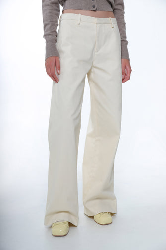 A woman wears a tan sweater and a full length cotton trousers in cream color, wide leg fit, and low waist with yellow shoes against a white background