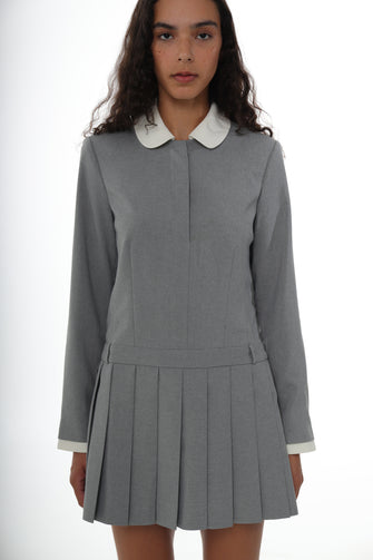 A woman wears a pleated mini dress in grey with a contrast white collar, long sleeves, and a side zipper against a white background