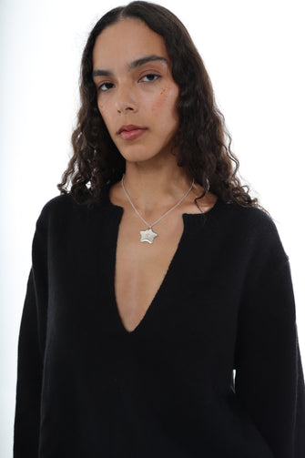 A woman wears a star necklace with a black v-neck sweater against a white background