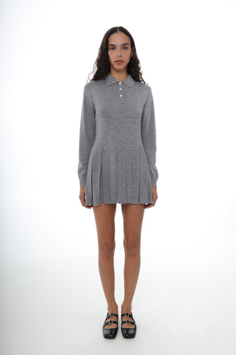 A woman wears a mini sweater dress in gray with long sleeves, a collar, and mother of pearl buttons with black shoes against a white background