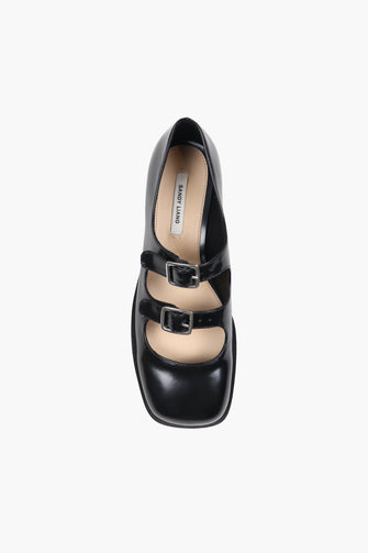 Black Mary Jane double strap shoes with a polished leather finish, featuring adjustable pin-buckle straps and a low heel against a white background