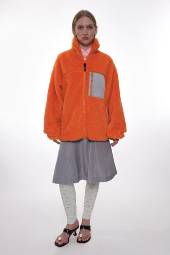 Person wearing an orange jacket and gray skirt on a white background