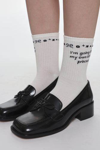 White socks with text reading "I'm going to be my own kind of princess" on the ankle with black shoes on a white background
