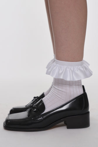 White socks with ruffles paired with black shoes on a neutral background