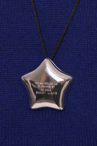 Star-shaped silver pendant on a black cord against a blue fabric background