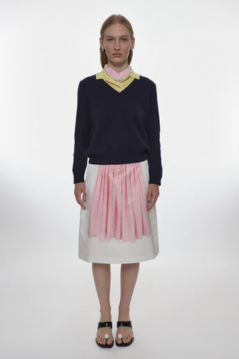 Person wearing a navy sweater with a yellow collar, white skirt with pink print on a white background