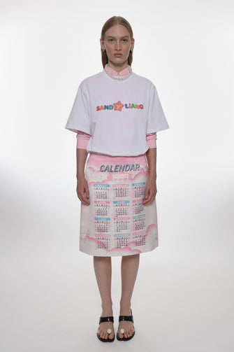 Model wearing a white oversized t-shirt with colorful text and a patterned skirt on a white background