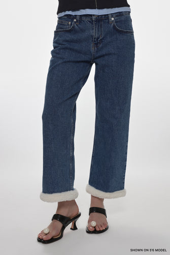 Person wearing blue jeans with white cuffs on a white background