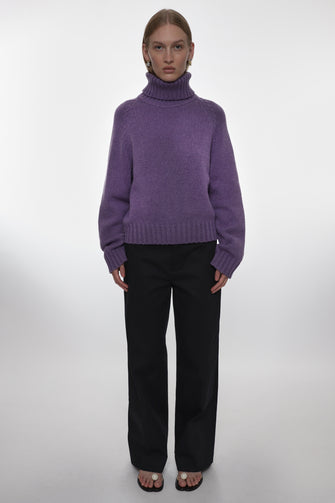 Person wearing a purple sweater and black pants on a white background