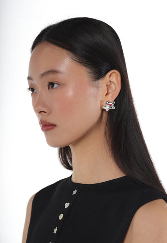 A woman wearing a star shaped silver stud earring against a white background