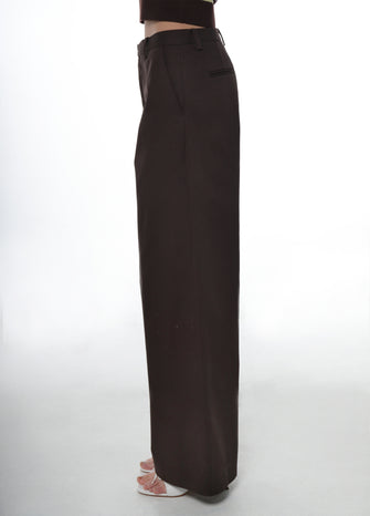 A woman wearing a brown pair of pants paired with white heels against a white background