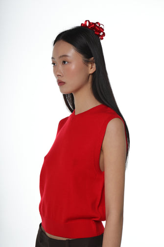 A woman wears a bright red shirt with a red bow in her hair against a white background