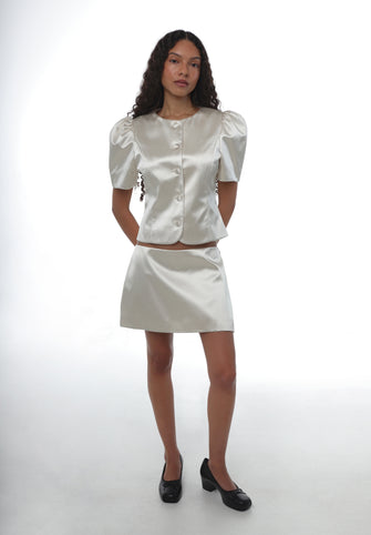 Woman wearing a champagne blouse and skirt set on a white background