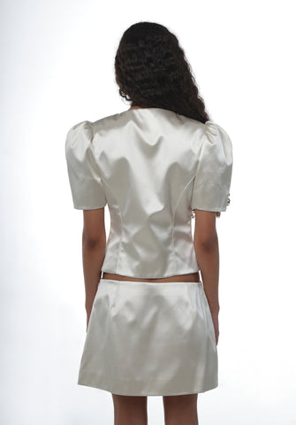 Person wearing a champagne satin jacket with puffed sleeves with a matching skirt on a white background