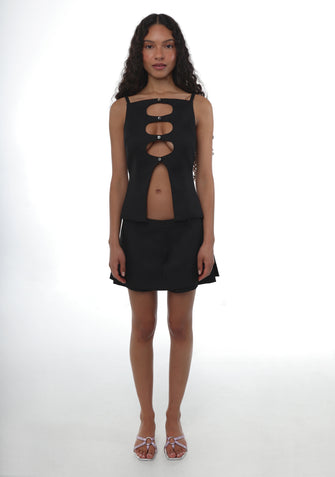 Woman wearing a black sleeveless top with cut outs on torso paired with a black mini skirt and sandals