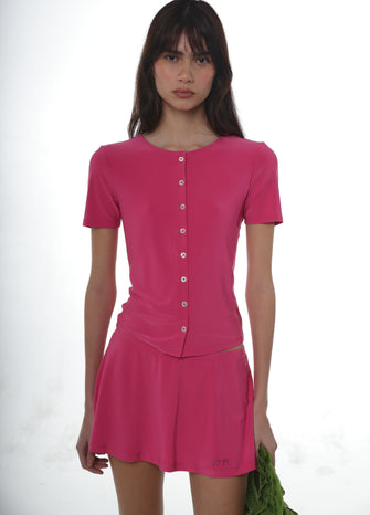 Woman wearing a pink jersey button up shirt and a pink jersey skort on a white background