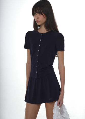 Woman wearing a navy short-sleeve button-up shirt with a navy skort on a white background