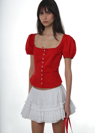 Woman wearing a red blouse with puff sleeves and a white ruffle skirt on a white background