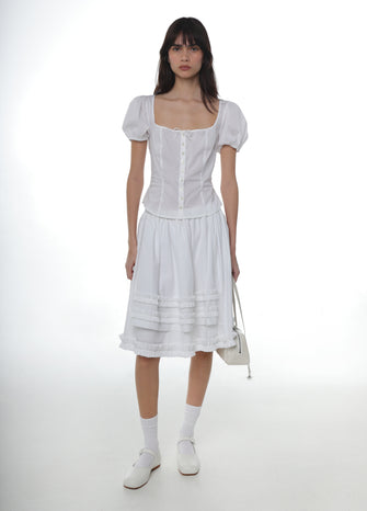 Woman wearing a white cotton shirt with puffed sleeves paired with a white cotton skirt with white socks and white mary janes and white bag
