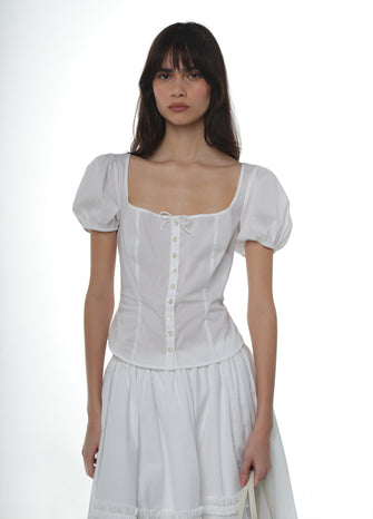 Woman wearing a white cotton shirt with puffed sleeves with a white cotton skirt on a white background