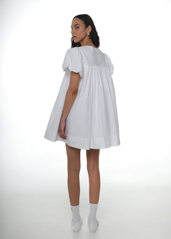 Woman wearing a white babydoll dress white crew socks and white mary jane shoes on a white background