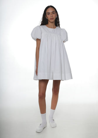 Woman wearing a white babydoll dress white crew socks and white mary jane shoes on a white background