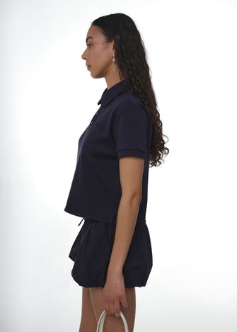 Person wearing a navy polo with navy bubble shorts on a white background