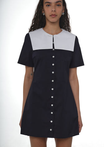 Woman wearing a navy cotton dress with button details and an oversized white sailor collar on a white background
