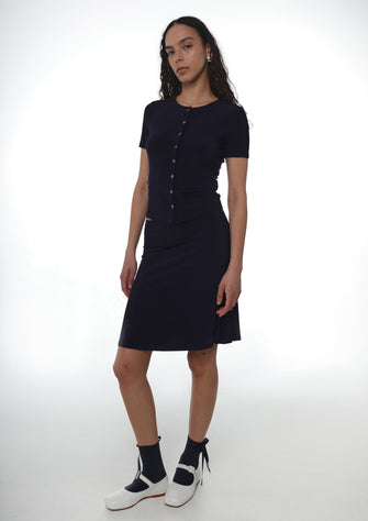 Woman wearing a navy jersey shirt with a matching jersey knee length skirt and navy socks with white shoes on a background