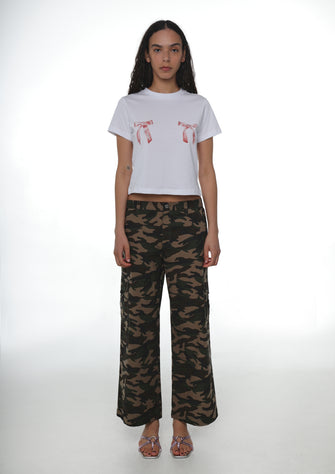 Person wearing a white t-shirt with bow graphic designs and camouflage pants on a white background