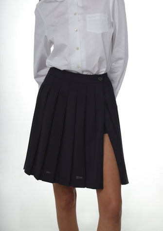 A close up of someone wearing a white peter pan collared shirt tucked into a navy pleated skirt against a white background