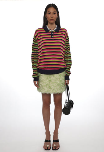 Model wearing a colorful striped sweater and green mohair skirt with a black handbag on a white background