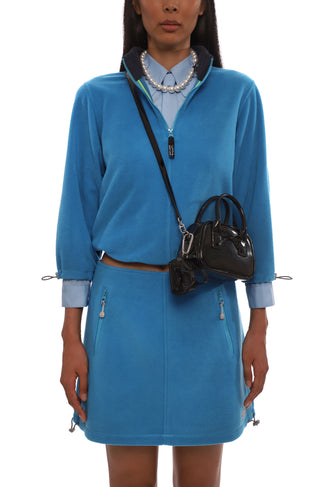 Woman wearing a blue fleece set with a black handbag on a white background