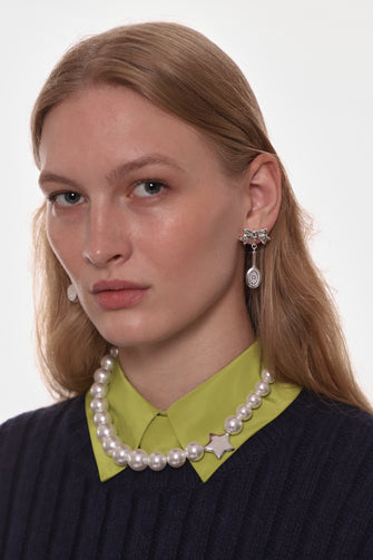 Woman wearing a pearl necklace and silver bow and hairbrush earrings against a white background