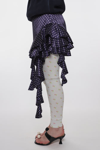 Person wearing a navy blue ruffled skirt over white leggings with a floral patterns on a white background