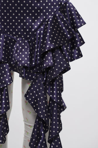 Navy blue dress with white polka dots and ruffled layers on a light gray background