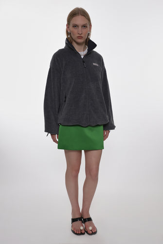 Person wearing a dark gray fleece pullover and green skirt on a white background