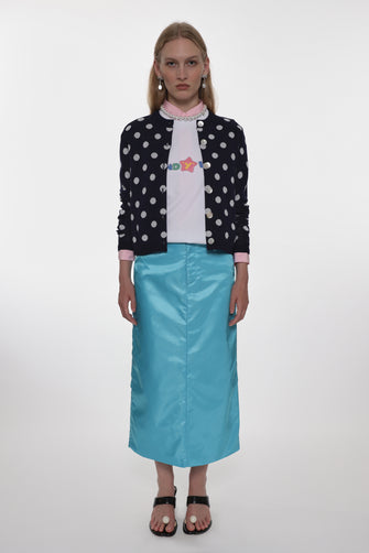 Person wearing a polka dot sweater, white shirt with a graphic, and blue skirt on a white background