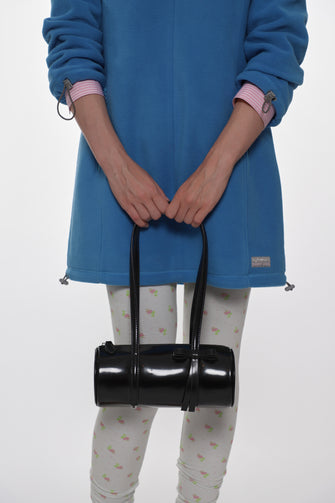 Person wearing a blue fleece dress with a black barrel shaped bag on a white background